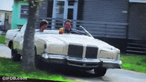 Two Men Are Driving A White Car Down A Road GIF