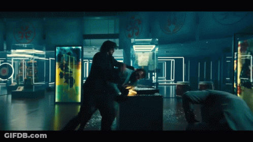 Two Men Are Fighting In A Dark Room With A Man Laying On The Floor GIF