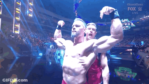Two Men Are Flexing Their Muscles In Front Of A Crowd At A Wrestling Match . GIF