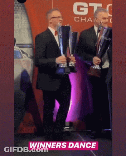 Two Men Are Holding Trophies In Front Of A Sign That Says Winners Dance GIF