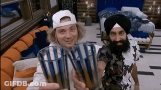 Two Men Are Holding Up Glasses In A Living Room GIF