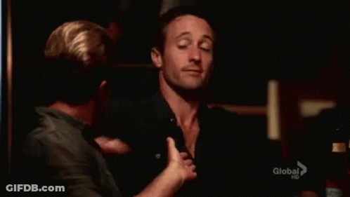 Two Men Are Hugging Each Other In A Dark Room And One Of Them Is Waving At The Camera . GIF