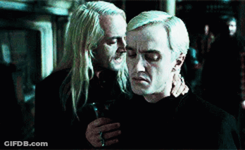 Two Men Are Hugging Each Other In A Dark Room . One Of The Men Is Holding A Glass Of Wine . GIF
