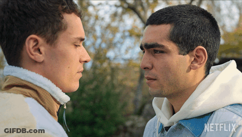 Two Men Are Looking At Each Other And One Has A Netflix Logo On His Shirt GIF