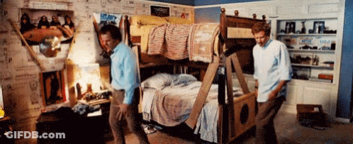 Two Men Are Moving A Bunk Bed In A Room With Posters On The Wall GIF