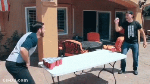 Two Men Are Playing A Game Of Beer Pong On A Table With Red Cups GIF