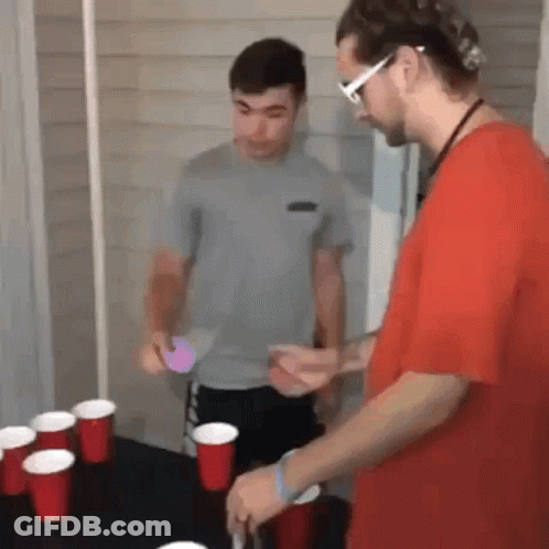 Two Men Are Playing A Game Of Beer Pong With Red Cups On The Table . GIF