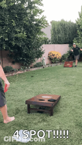 Two Men Are Playing A Game Of Cornhole In A Backyard And One Of Them Is Holding A Frisbee . GIF