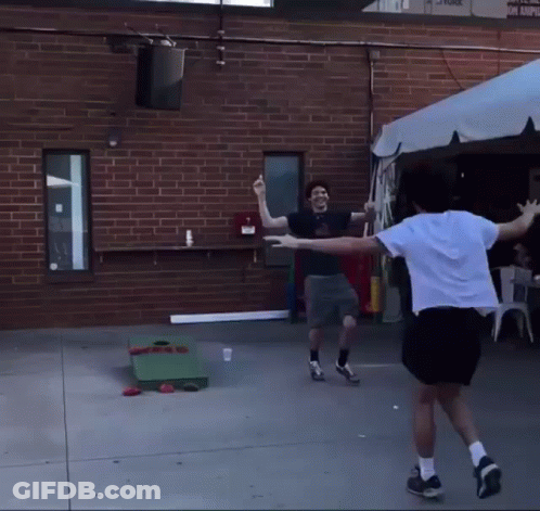 Two Men Are Playing A Game Of Cornhole In Front Of A Building GIF
