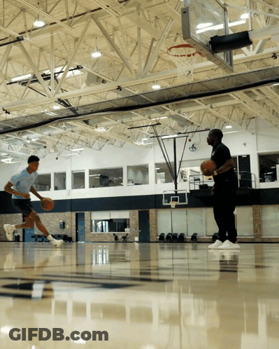 Two Men Are Playing Basketball In A Gym With A Hoop In The Background GIF