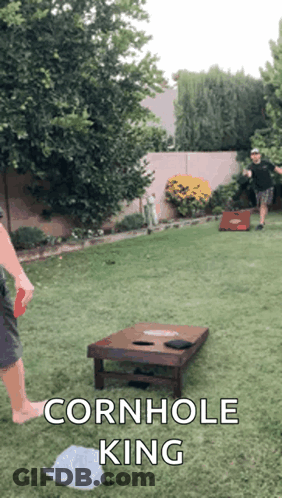 Two Men Are Playing Cornhole In A Backyard With The Caption " Cornhole King " On The Bottom GIF