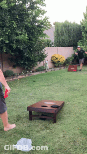 Two Men Are Playing Cornhole In The Backyard GIF