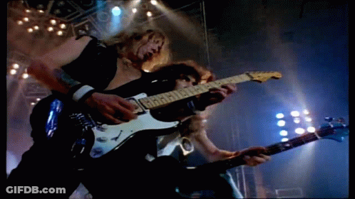 Two Men Are Playing Guitars On A Stage And One Of Them Is Wearing A Black Vest GIF