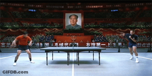 Two Men Are Playing Ping Pong In Front Of A Picture Of Mao Zedong On The Wall GIF