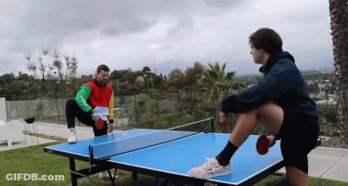 Two Men Are Playing Ping Pong On A Table That Says Wilson GIF