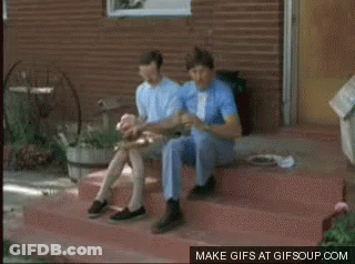 Two Men Are Riding A Bicycle On A Dirt Road With Mountains In The Background GIF
