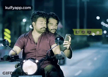 Two Men Riding Motorcycle One Looking At Phone GIF
