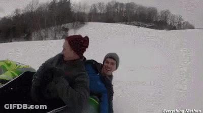 Two Men Are Riding A Sled Down A Snowy Hill GIF