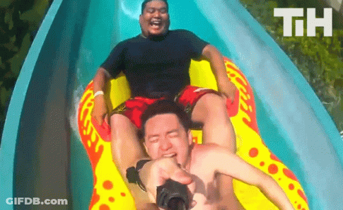 Two Men Are Riding Down A Water Slide With The Letters Th Visible In The Background GIF