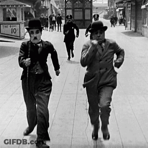 Two Men Are Running Down A Street In Front Of A Sign That Says The Boss 10 Cents GIF