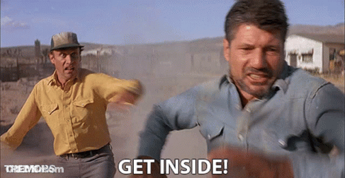 Two Men Are Running In A Dirt Field And One Of Them Is Saying Get Inside GIF