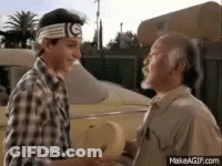 Two Men Are Shaking Hands In Front Of A Car . One Of The Men Is Wearing A Headband With The Letter G On It . GIF
