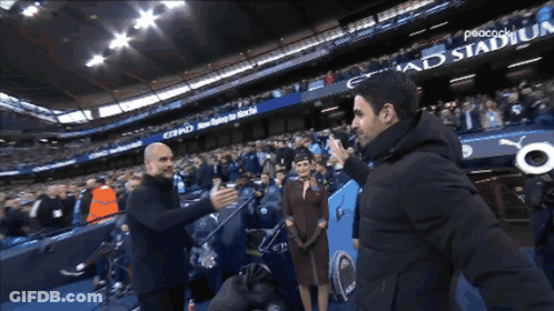 Two Men Are Shaking Hands In Front Of A Peacock Stadium Banner GIF