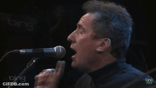 Two Men Are Singing And Playing Keyboards In Front Of A Bing Sign GIF