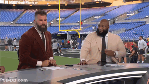 Two Men Are Sitting At A Desk In Front Of A Stadium That Says M & T Bank Stadium GIF