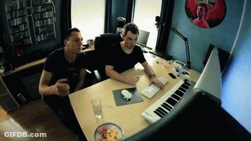 Two Men Are Sitting At A Desk With A Keyboard GIF