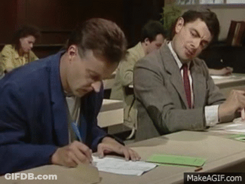Two Men Are Sitting At A Desk Writing On A Piece Of Paper In A Classroom . GIF