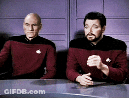 Two Men Are Sitting At A Table And One Has A Badge On His Shirt That Says ' Captain ' GIF