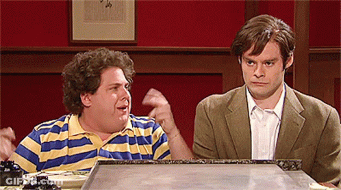 Two Men Are Sitting At A Table And One Has A Striped Shirt On GIF