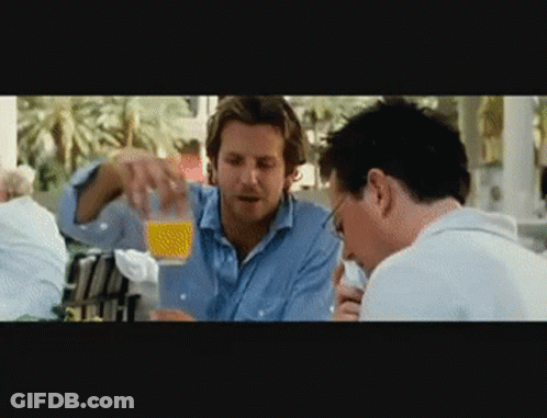 Two Men Are Sitting At A Table And One Is Pouring Orange Juice Into Another Man 'S Glass GIF