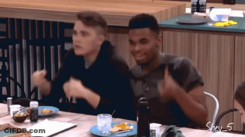 Two Men Are Sitting At A Table And One Of Them Is Wearing A Shirt That Says One On It GIF