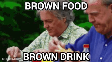 Two Men Are Sitting At A Table Eating Food And Drinking Brown Drinks GIF