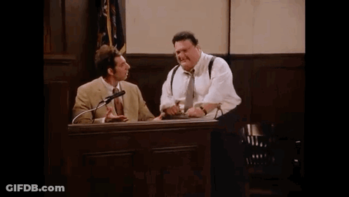 Two Men Are Sitting At A Table In A Courtroom Talking Into Microphones . GIF