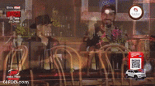 Two Men Are Sitting At A Table In A Restaurant Talking To Each Other GIF