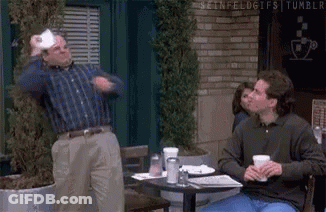 Two Men Are Sitting At A Table In Front Of A Brick Building . GIF