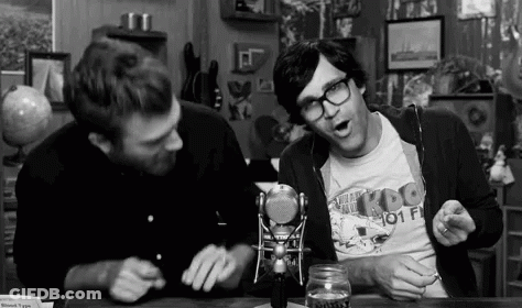 Two Men Are Sitting At A Table In Front Of A Microphone Talking To Each Other . GIF