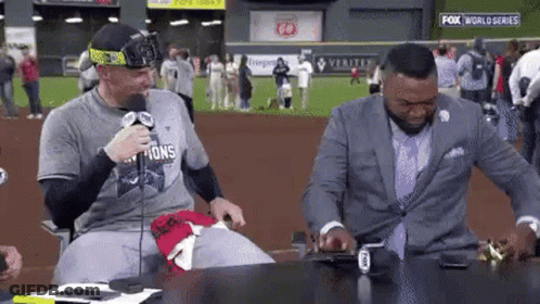 Two Men Are Sitting At A Table In Front Of A Microphone . GIF