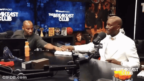 Two Men Are Sitting At A Table In Front Of A Sign That Says The Breakfast Club GIF