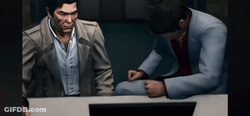 Two Men Are Sitting At A Table Looking At A Computer Screen . GIF