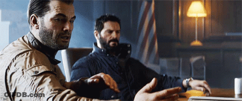 Two Men Are Sitting At A Table Looking At A Laptop Computer GIF