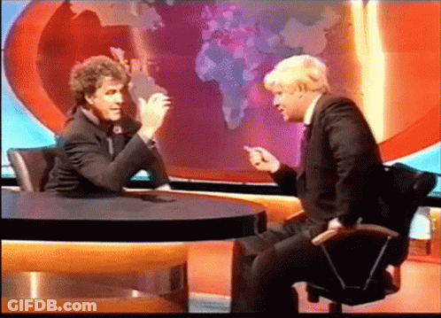 Two Men Are Sitting At A Table Talking In Front Of A World Map GIF