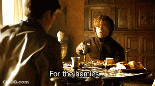 Two Men Are Sitting At A Table Talking To Each Other And One Of Them Is Holding A Glass Of Wine . GIF