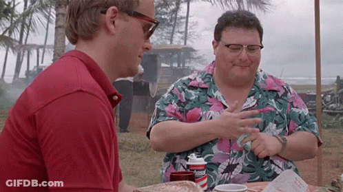 Two Men Are Sitting At A Table Talking To Each Other . One Of The Men Is Wearing Sunglasses . GIF