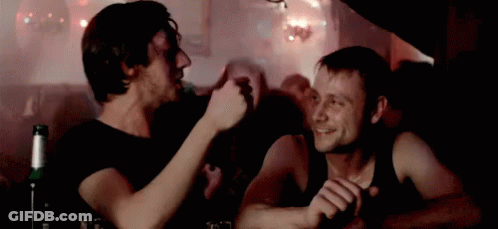 Two Men Are Sitting At A Table With A Bottle Of Beer In The Foreground . GIF