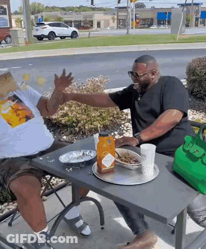 Two Men Are Sitting At A Table With A Bottle Of Tabasco Ketchup On It GIF