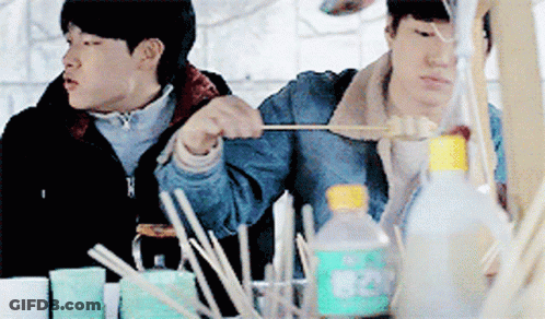 Two Men Are Sitting At A Table With A Bottle That Says 820 GIF